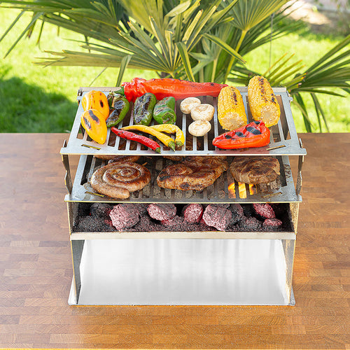 Holzkohlegrill aus Edelstahl mit 2 übereinander platzierte Grillroste und reichlich Fleisch und buntem Gemüse darauf.