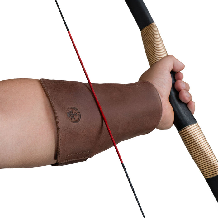 Valhalla Gear Archery Arm Guard featured on a hand ready to shoot an arrow, showcasing its effective design as a forearm protector. This essential item for any archer is made from fire branded full grain leather, representing small batch production and expert craftsmanship in La Antigua Guatemala.