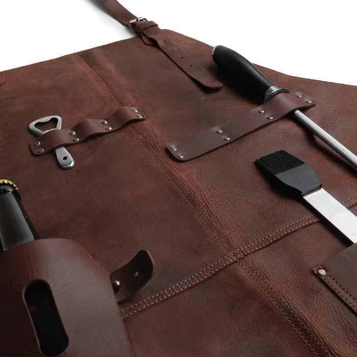 Detailed view of Cast Leather Co. BBQ Apron, showcasing pockets and tools, emphasizing its rustic charm. Made from full grain leather, this artisan BBQ Apron is designed for cooking with convenience, exemplifying small batch, hand cut, and hand sewn production.
