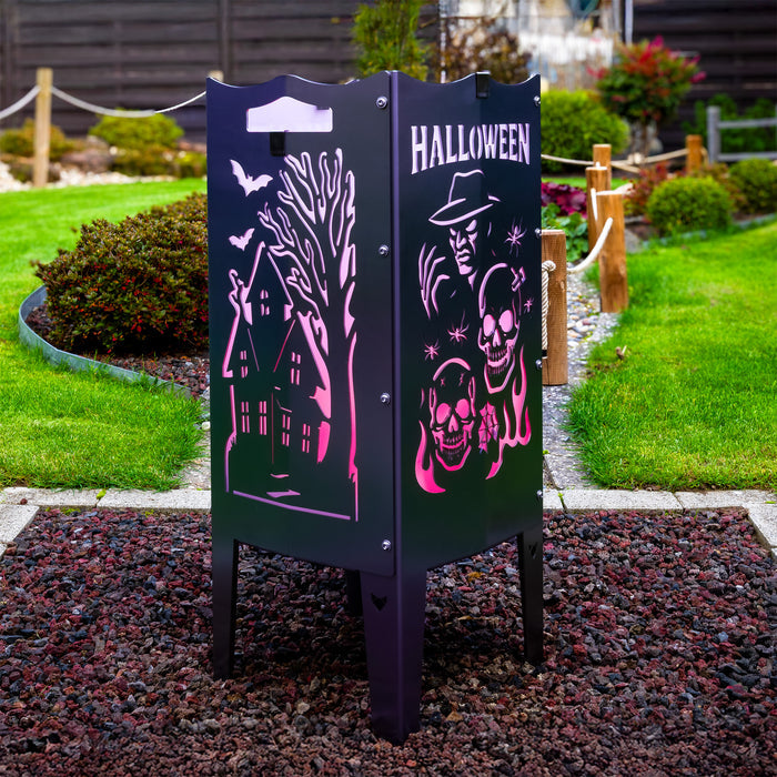 Die FENNEK Feuersäule aus Edelstahl mit Halloween Motiv steht auf einem Kiesbett in einem schönem Garten. Die Feuersäule leuchtet dank des LED Lichtersets lila. So schafft sie auch ganz ohne Feuer eine tolle Atmosphäre.
