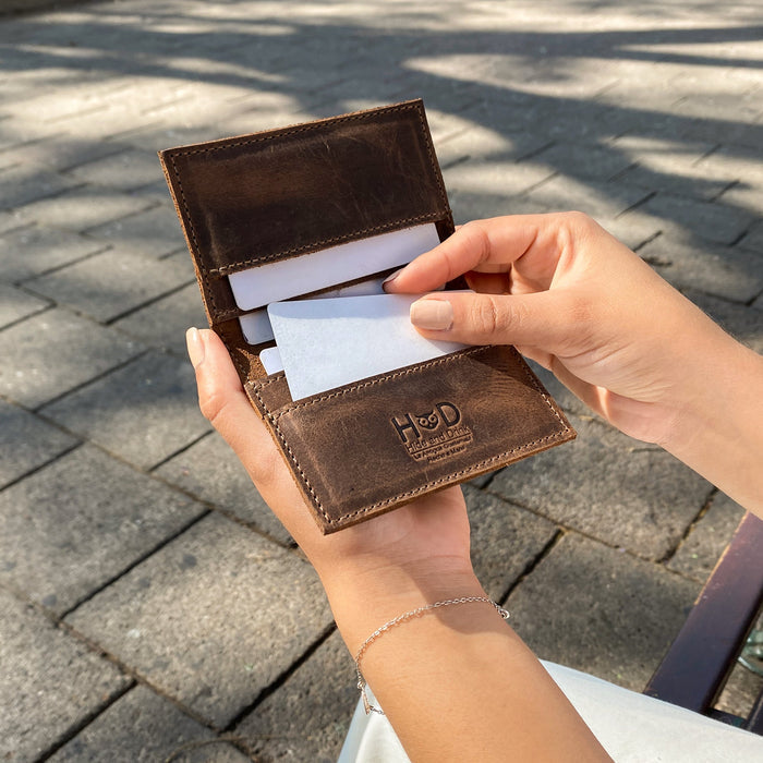 Bifold Horizontal Card Wallet by Hide & Drink being held, demonstrating its practical use as a minimalist traveller wallet, designed as an organizer to hold up to 8 cards, made from high-quality full grain leather, showcasing small batch production, hand cut, hand sewn, fire branded artistry, handmade in La Antigua Guatemala & Oaxaca Mexico.