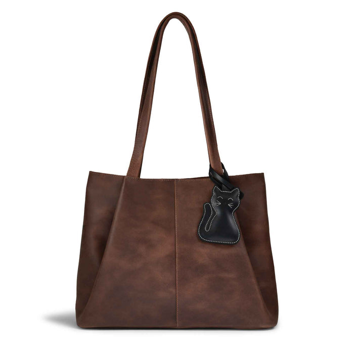 Hide & Drink Bag Charms attached to a stylish brown handbag, showcasing a golden cat design perfect for personalization. This purse charm for tote & backpacks is made from high-quality full grain leather, representing StockyardX's focus on small batch production with hand cut, hand sewn details and fire branding, handmade in La Antigua Guatemala & Oaxaca Mexico.