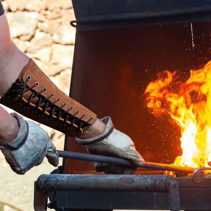 The Blacksmith Forearm Protector by Toolshed Hide being used during blacksmithing, highlighting its durability and heat resistance feature. Crafted from full grain leather, this rustic bracer offers protection and is a testament to small batch production and artisan craftsmanship.