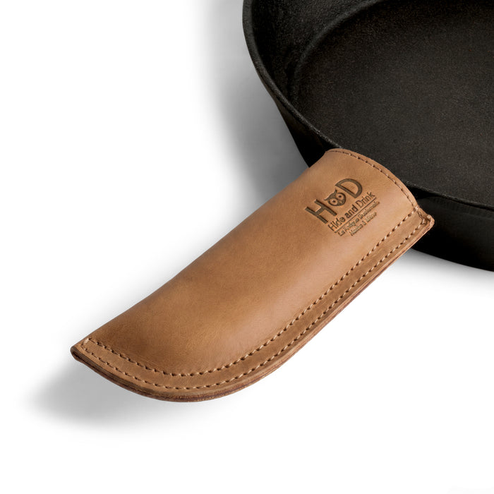 Hide & Drink Cast Iron Panhandle Cover elegantly modeled on a skillet. This artisan piece serves as a hot handle protector, made from durable full grain leather and features double stitched craftsmanship. Hand cut and sewn in La Antigua Guatemala & Oaxaca Mexico, it enhances kitchen safety and style.