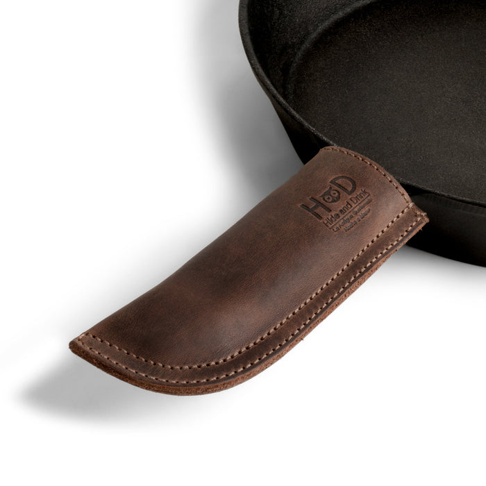 Hide & Drink Cast Iron Panhandle Cover showcasing a handmade full grain leather design, perfect as a hot handle protector. This double stitched, artisan potholder easily slides on and off metal skillets, blending functionality with style. Crafted in La Antigua Guatemala & Oaxaca Mexico, it's part of a small batch production and features fire branded artistry.