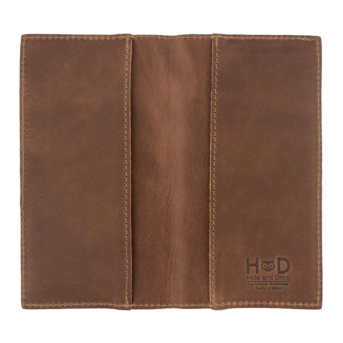 Checkbook Leather Cover by Hide & Drink in a rich brown shade, designed to function as a minimalist organizer for standard checkbooks. This artisan product, handmade from full grain leather, highlights craftsmanship from La Antigua Guatemala and Oaxaca Mexico, emphasizing small batch production.