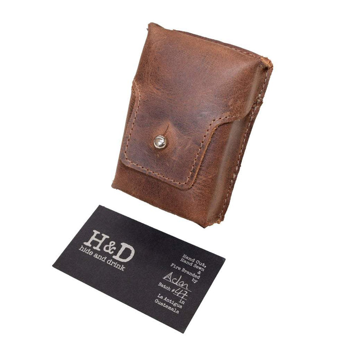 Hide & Drink's Cigarette Pack Cover beside its business card, emphasizing its quality and handmade nature. This Full Grain Leather holder is crafted with care, perfect for those seeking elegant and functional accessories.