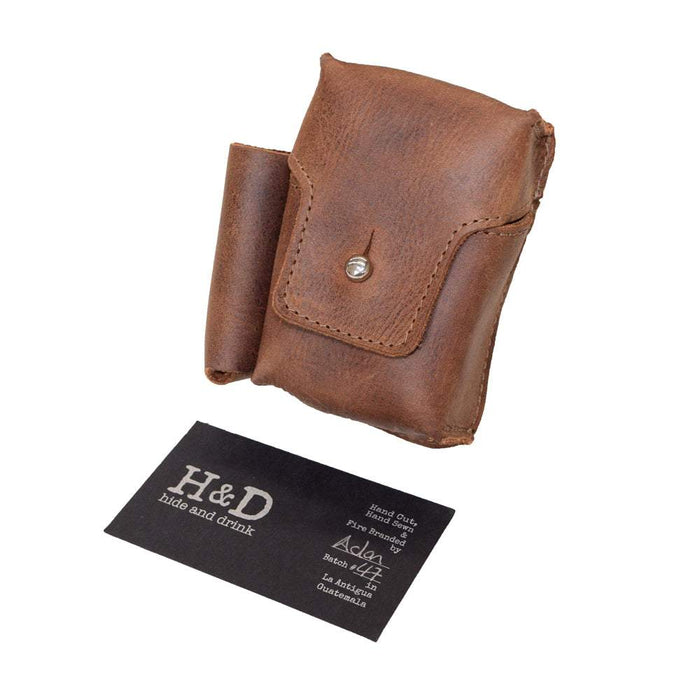 Hide & Drink Cigarette Pack & Lighter Cover next to a business card, highlighting the artisan quality and durable Full Grain Leather. This accessory is perfect for smokers, crafted using small batch production in La Antigua Guatemala & Oaxaca Mexico.