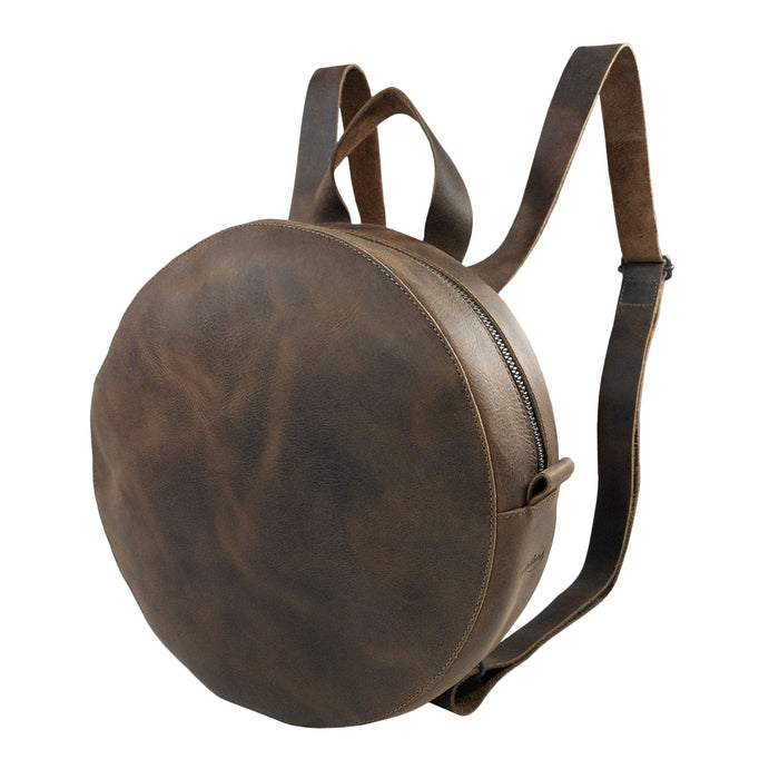 Heather's Circular Backpack featuring a round, full grain leather design, perfect as a travel accessory or casual daypack. This backpack includes adjustable straps and showcases the craftsmanship of small batch production, being hand cut and hand sewn by artisans in La Antigua Guatemala & Oaxaca Mexico.