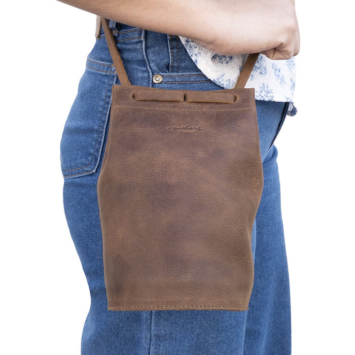 A person wearing Heather's Cylinder Shoulder Phone Bag, a trendy cylinder-shaped purse with an adjustable shoulder strap. Crafted from full grain leather, this crossbody bag showcases the artisan skills from StockyardX, featuring small batch production and hand cut, hand sewn details. Handmade in La Antigua Guatemala & Oaxaca Mexico.