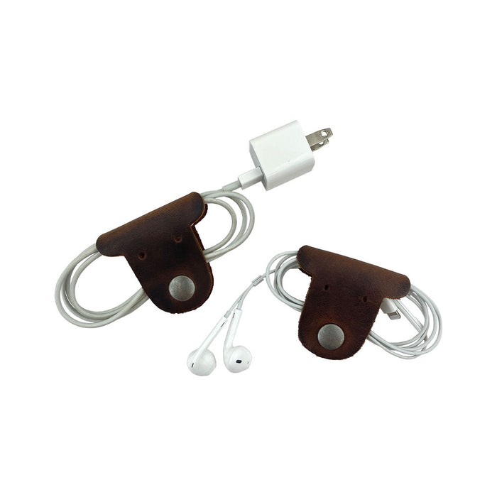 Two dark brown Dog Shaped Cord Keepers neatly organizing earbuds and a charging cord, highlighting the playful design by Hide & Drink. Dog Shaped Cord Keeper (Cord Clam) 2-Pack, Full Grain Leather, StockyardX, Small Batch Production, Hand Cut, Hand Sewn, Fire Branded, Artisan, Handmade in La Antigua Guatemala & Oaxaca Mexico.