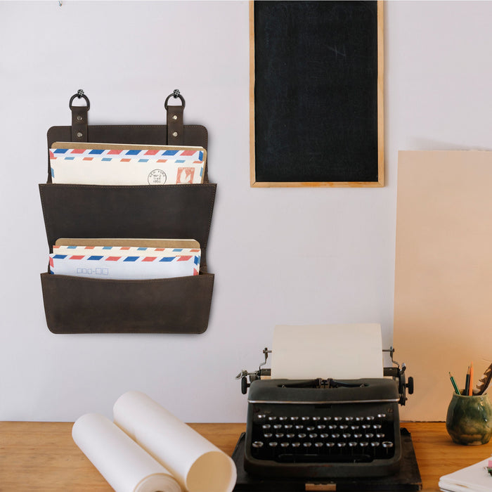 Hide & Drink Double Document Holder for Hanging mounted on a wall, adorned with letters, demonstrating its role as stylish wall mount file storage. Constructed with quality full grain leather, this item is a testament to artisan craftsmanship, small batch production, hand cut, hand sewn, and fire branded, handmade in La Antigua Guatemala & Oaxaca Mexico.