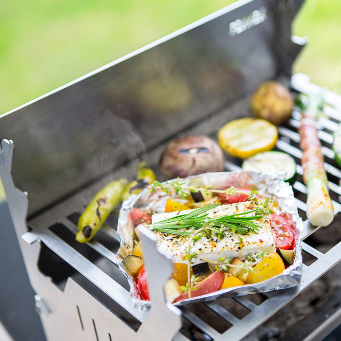 Bild zeigt den FENNEK Grill in Betrieb.  Auf dem Grillrost brutzelt unter anderem Gemüse, Fleisch und Schafskäse vor sich hin.