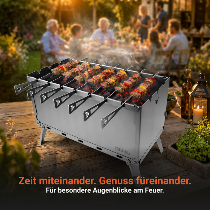 FENNEK Mangal Grill mit bestückten Fleischspießen auf einem Holztisch vor einer feiernden Familie im Hintergrund