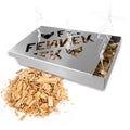 FENNEK Räucherbox gefüllt mit Hackschnitzel, welche bereits etwas qualmen. Vorne links vor der Box liegen weitere Hackschnitzel.