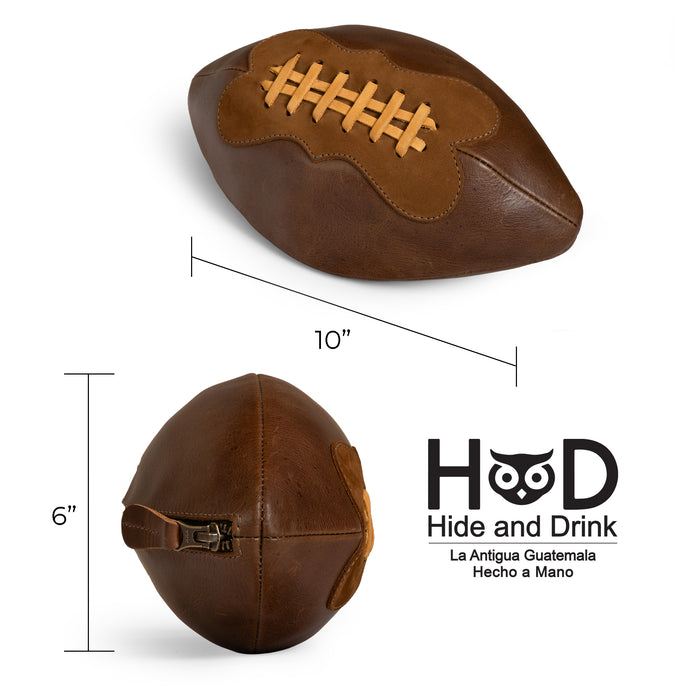 Measuring dimensions displayed next to the Football Toiletry Bag by Hide & Drink, emphasizing its compact size. This Gameday Football Dopp Toiletry Bag is made from full grain leather, making it an excellent travel organizer and a sturdy bag for grooming essentials or shaving kits. Handmade with love in La Antigua Guatemala, it reflects the artisan craftsmanship of small batch production.