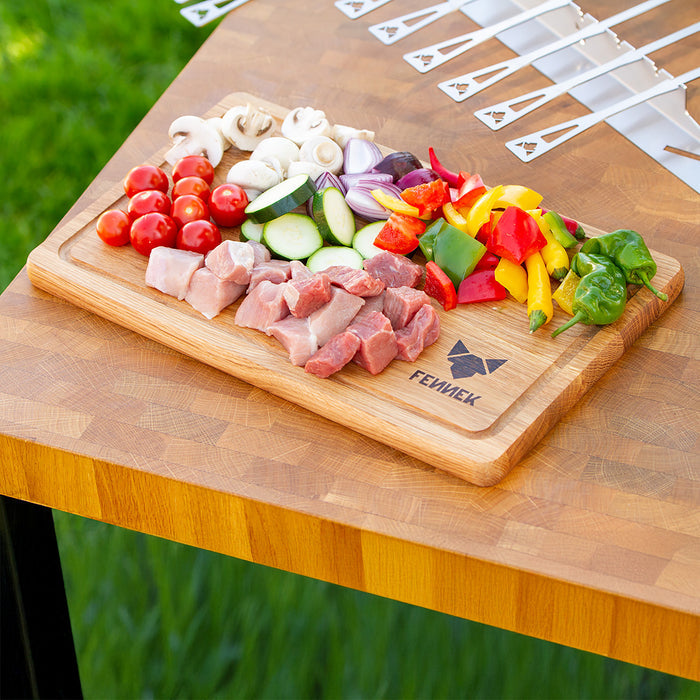 Vorbereitetes, kleingeschnittenes buntes Gemüse und Fleisch auf dem Schneidebrett aus Holz mit FENNEK Logo-Branding rechts unten.