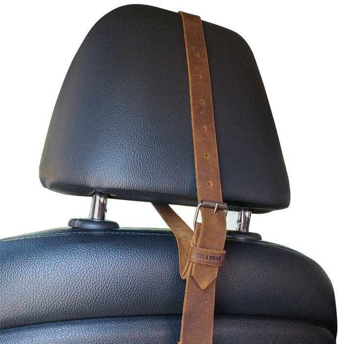 View of the Hat Hanger by Hide & Drink on a car seat, demonstrating its adjustable height and minimalist style. This travel accessory made from full grain leather is perfect for organization while on the go, reflecting handmade quality from La Antigua Guatemala & Oaxaca Mexico.