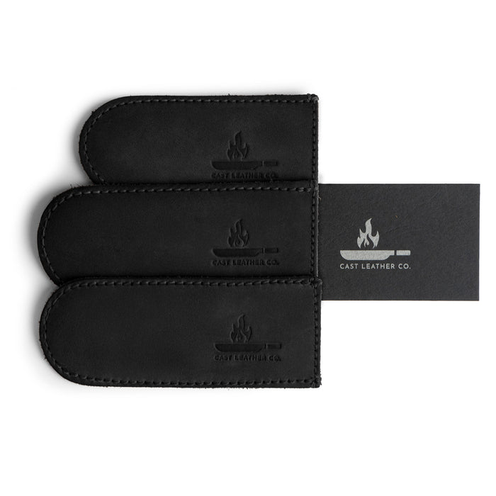 The black Hot Handle Covers (Set of 3) from Cast Leather Co. displayed with included business card, highlighting handmade quality. These full grain leather skillet handle covers combine functionality with style, showcasing the brand's commitment to artisan craftsmanship.