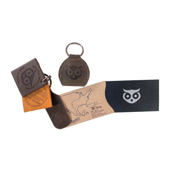 Flat lay of the Key Chain & Guitar Pick Holder by Hide & Drink with packaging materials. This Guitar Pick Holder with Ring is designed as a key organizer for guitar players, made from Full Grain Leather. Showcasing small batch production techniques, it is Hand Cut and Hand Sewn with a fire branded logo, handmade in La Antigua Guatemala & Oaxaca Mexico.