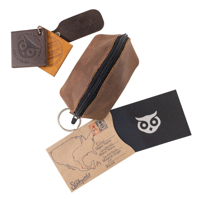 Hide & Drink’s Keychain Coin Pouch alongside branding elements and a care tag, emphasizing its handcrafted quality. Coin Pouch, Keychain, Wallet, Purse, Holder, SD Card, USB, Cash, Case, made of Full Grain Leather, handmade in La Antigua Guatemala & Oaxaca Mexico.