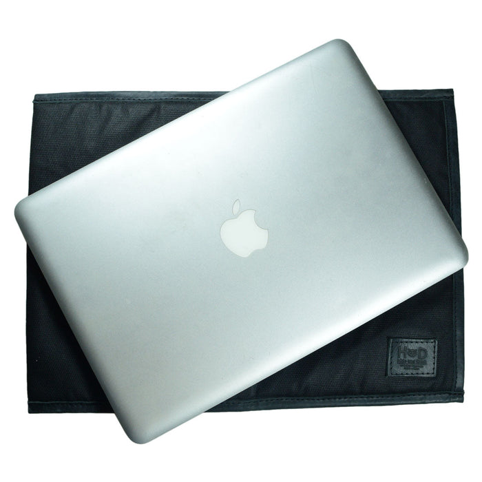 Overhead view of Laptop Sleeve 14 in. by Hide & Drink with a MacBook on top. This stylish and rugged sleeve is compatible with MacBook Air/Pro 13 Inch with M1 Chip, handcrafted from Waxed Canvas, ensuring durability through small batch production, hand cut, hand sewn, and fire branded techniques by artisans in La Antigua Guatemala & Oaxaca Mexico.