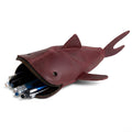 Hide & Drink Leather Shark Pouch filled with pens, showcasing its style and functionality as a zippered coin pouch, change bag, pencil purse, scissors case, and shark-shaped cable holder. Crafted from full grain leather, this artisan-made pouch demonstrates careful hand cut and hand sewn techniques, embodying small batch production from La Antigua Guatemala & Oaxaca Mexico.