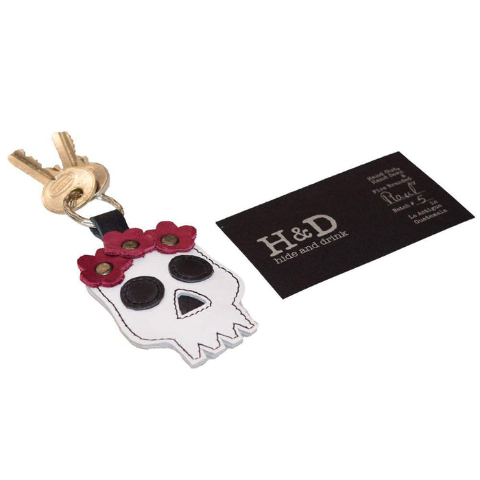 Showing the Mexican Skull Keychain by Hide & Drink alongside a business card, illustrating its artisanal quality and unique design. This key ring, ideal for Dia de los Muertos, is crafted from Full Grain Leather with attention to detail, representing the best of handmade goods from La Antigua Guatemala & Oaxaca Mexico.