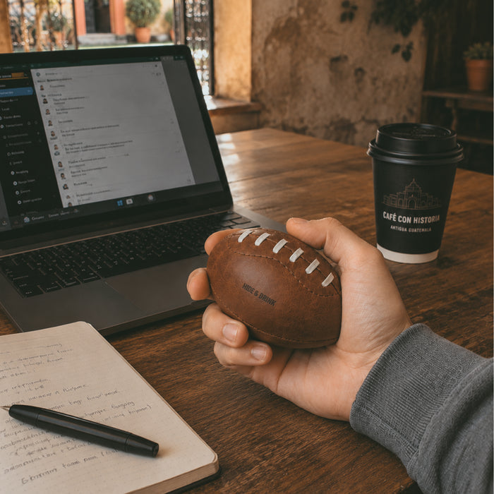 A hand gripping a Mini American Football by Hide & Drink, illustrating its perfect fit and unique shape. Made from high-quality full grain leather, this handstitched football is a memorable decorative item and an artisan keepsake, made in La Antigua Guatemala & Oaxaca Mexico.