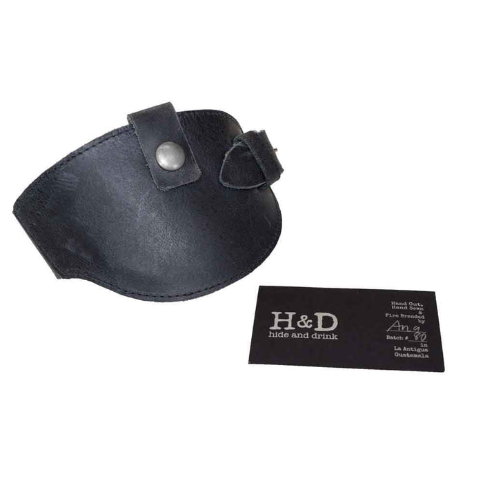 Motorcycle Boot Protector in black from Hide & Drink, highlighted with a business card showcasing its artisan production. This product offers essential protection for your shoes from the shifter, made from high-quality full grain leather, reflecting the small batch craftsmanship from La Antigua Guatemala.