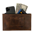 A brown rectangular zippered handbag by Hide & Drink, designed for women, featuring a card slot and filled with cash and a smartphone. This stylish female purse is crafted from durable full grain leather, and showcases the artisan craftsmanship with small batch production that's hand cut and sewn. A practical yet elegant accessory made in La Antigua Guatemala & Oaxaca Mexico.