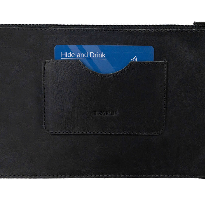 Close-up view of a black rectangular zippered handbag by Hide & Drink, emphasizing the card slot. This female purse is crafted from durable full grain leather, ensuring quality. Highlighting artisan craftsmanship, it is handmade with care in small batch production, made in La Antigua Guatemala & Oaxaca Mexico.