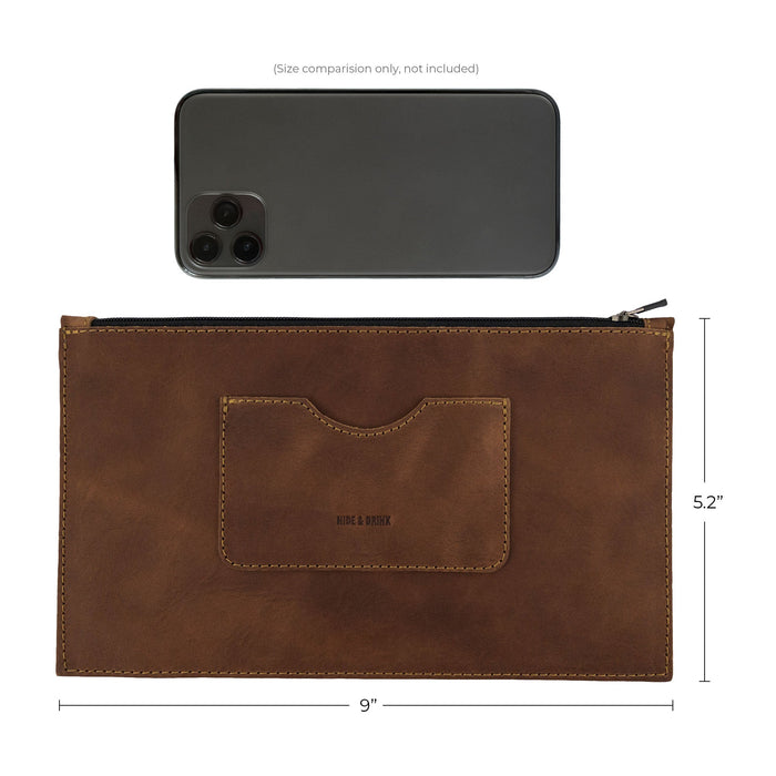 Size comparison of a brown rectangular zippered handbag by Hide & Drink next to an iPhone, illustrating its dimensions. Designed for women, this full grain leather female purse features a card slot, emphasizing artisan crafting through small batch production, handmade in La Antigua Guatemala & Oaxaca Mexico.
