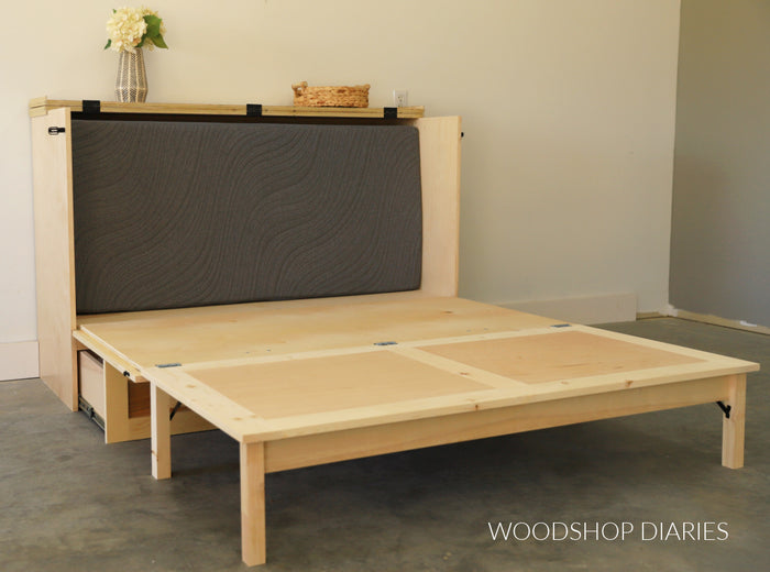 DIY murphy bed cabinet folded out showing plywood bed platform and fold-down legs