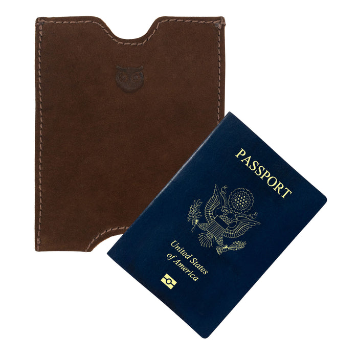 Hide & Drink Passport Sleeve next to a blue passport, showcasing its snug fit and vintage design. This Full Grain Leather Travel Passport Pocket Sleeve is expertly handcrafted and fire branded.