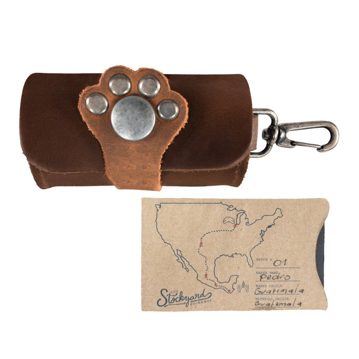 Taco Dog Paw Poop Bag Pouch next to a unique artisan tag, highlighting the small batch production from La Antigua Guatemala. This stylish full grain leather carrier clips onto leashes and offers easy disposal during dog walks, emphasizing quality and practicality.
