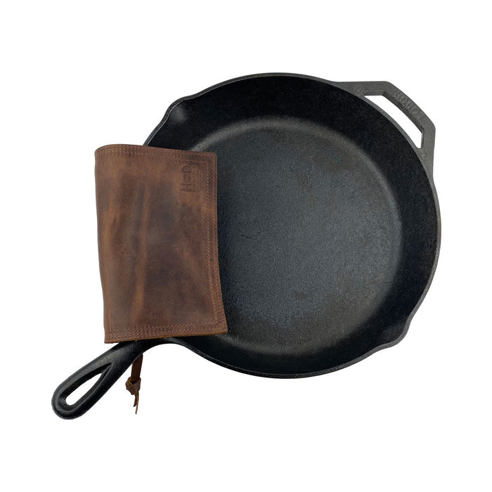 Hide & Drink Pot Pad next to a cast iron skillet in use. This double-layered rustic leather pot pad is perfect for handling hot cookware safely and stylishly.