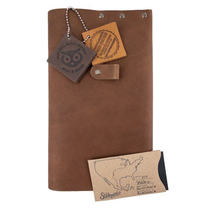 The Riveted Journal Cover (5 x 8.50 in.) by Hide & Drink displayed with care instructions and tags. This artisan handmade product showcases full grain leather and embodies the vintage style typical of small batch production from La Antigua Guatemala and Oaxaca Mexico.