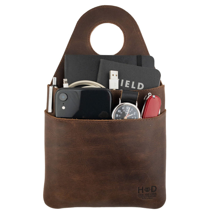 Hide & Drink's Seat Side Organizer for Gear Stick filled with essentials like chargers and small items, made from premium Full Grain Leather. This holder is not only practical for organizing but also an outdoor protector for knives. It's a handmade product created through small batch production, emphasizing hand cut, hand sewn quality by artisans in La Antigua Guatemala & Oaxaca Mexico.