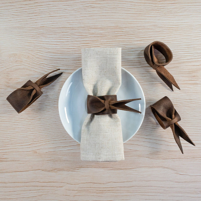 Stylish Set of 4 Napkin Rings for Weddings by Hide & Groom, featuring leather napkin rings styled with bows on a plate setting. Ideal for dinner parties and wedding decorations, made from full grain leather, highlighting artisan craftsmanship from small batch production in La Antigua Guatemala & Oaxaca Mexico.
