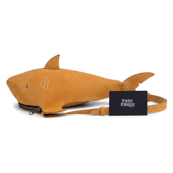 The Shark-Shaped Shoulder Bag by Tudi Frudi displayed alongside its branding card. This eye-catching accessory, made from premium Full Grain Leather, is a testament to artisan craftsmanship with its hand sewn details, adjustable strap, and versatile use as a crossbody or messenger bag.