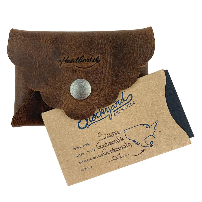 Stylish Envelope by Heather's displayed with its artisan tag describing the craftsmanship and origin. This classy organizer offers compact storage for debit and credit cards, made from full grain leather, showcasing small batch production methods, hand cutting, hand sewing, and fire branding, handmade in La Antigua Guatemala & Oaxaca Mexico.