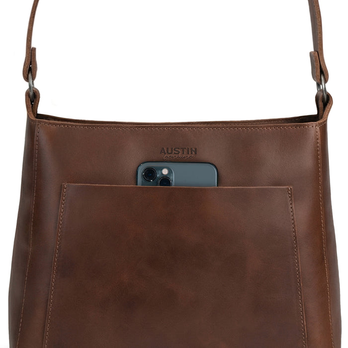 The Allandale Tote Bag by Austin Genuine, highlighting its exterior pocket holding a phone. Made of full grain leather, this artisan tote is a result of small batch production, hand cut and hand sewn techniques, and is fire branded, handmade in La Antigua Guatemala & Oaxaca Mexico.
