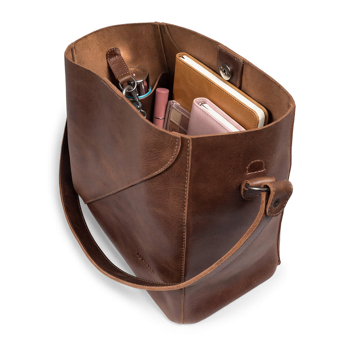 Top-down view of The Pemberton Shoulder Bag by Austin Genuine filled with essentials, highlighting its practical functionality and artisan quality, crafted from full grain leather.
