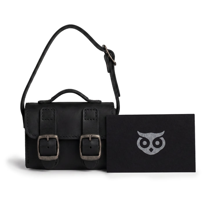 The Black Tiny Messenger Bag by Hide & Drink, featured with accompanying tags. This Mini Messenger Bag Charm, crafted from quality Full Grain Leather, serves as an elegant keychain or handbag accessory. Artisan-made in La Antigua Guatemala, reflecting small batch craftsmanship.