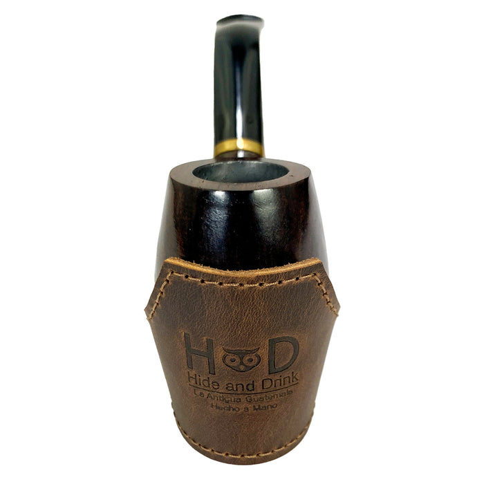 Close-up of the Tobacco Pipe Holder by Hide & Drink with a pipe and tobacco on a leather surface. This Tobacco Pipe Holder (Pipe not Included) serves as a portable & adjustable stand, enhancing your smoking accessories collection. Crafted from full grain leather through small batch production, it's a handmade, fire branded product from artisans in La Antigua Guatemala & Oaxaca Mexico.