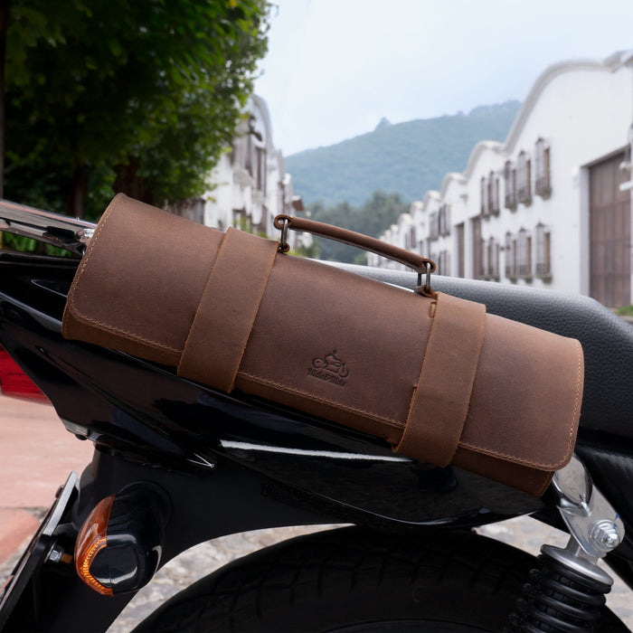 Tool Roll for Bikers displayed on a motorcycle seat, showcasing the stylish brown leather design by Hide & Ride. This Motorcycle Tool Bag doubles as a Universal Saddlebag for Motorcycle and Fork Bag for Bikers, emphasizing exquisite Full Grain Leather craftsmanship. Discover the quality of Small Batch Production with Hand Cut and Hand Sewn finishes, made by talented artisans in La Antigua Guatemala & Oaxaca Mexico.