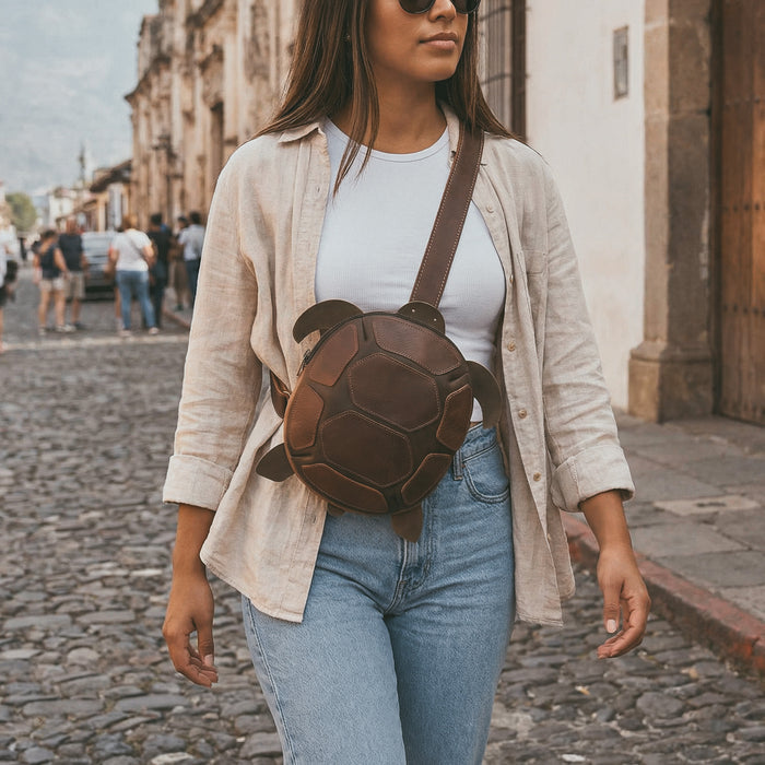Lifestyle image featuring the Leather Turtle-Shaped Crossbody Bag by Hide & Play being worn casually. This turtle-shaped messenger bag is crafted from full grain leather, making it a stylish accessory for travel. Handmade in La Antigua Guatemala & Oaxaca Mexico, this bag combines functionality with small batch artisan craftsmanship.