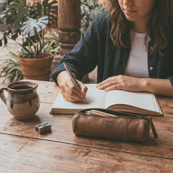 Utility Cylinder Case by Hide & Drink shown with pens, ideal for organizing stationery or personal items. This classic bag is handmade from Full Grain Leather, crafted in small batches in La Antigua Guatemala. Cylinder Case, Handmade, Rustic.
