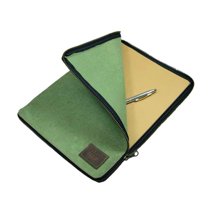 Open view of the Waxed Canvas Zippered Journal Cover for Moleskine (Notebook NOT Included) by Hide & Drink, showcasing a green Canvas interior with a pen. Ideal for Cahier Cases, features Full Grain Leather, Hand Cut, Hand Sewn craftsmanship, and is made by artisans in La Antigua Guatemala & Oaxaca Mexico.